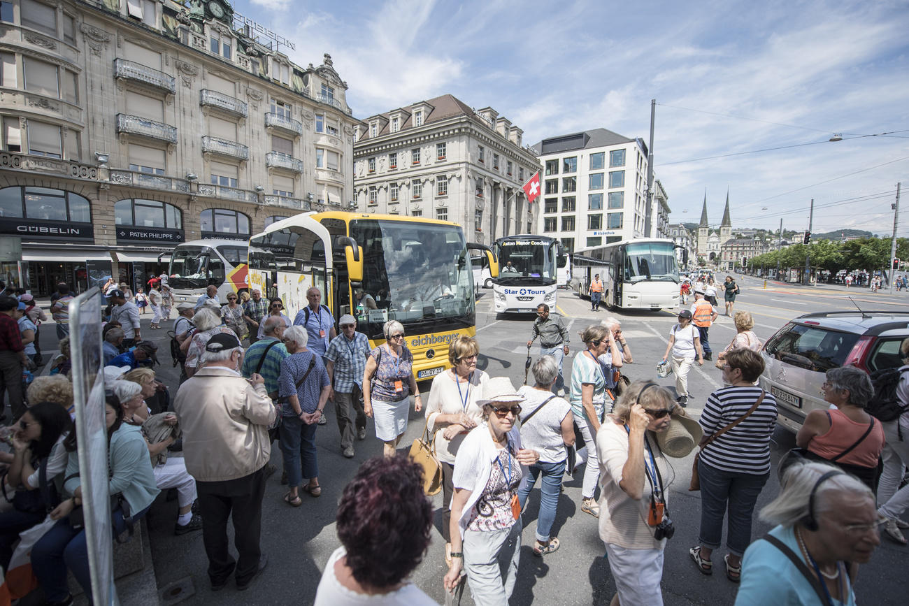 immagine di una piazza cittadina con pullman parcheggiati e persone che scendono.