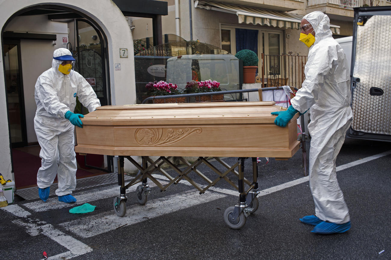 dos hombres con trajes contra virus sacan un féretro de un vehículo