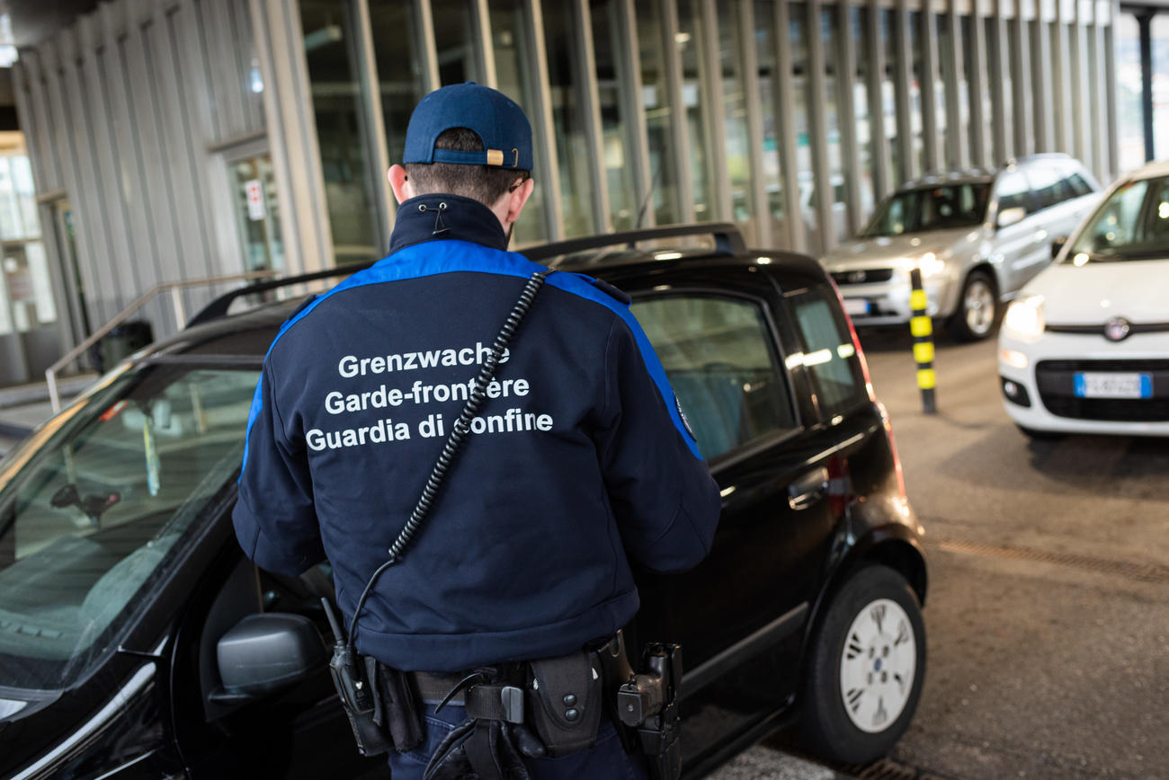 Guardia di confine ripresa di schiena in un posto di frontiera; si vedono sfocate auto con targhe italiane