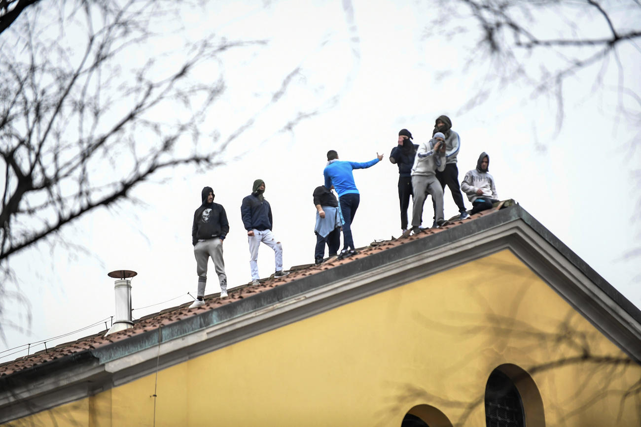 Gruppo di otto uomini su un tetto di vecchio edificio giallo con grandi vetrate e grate; visti da lontano