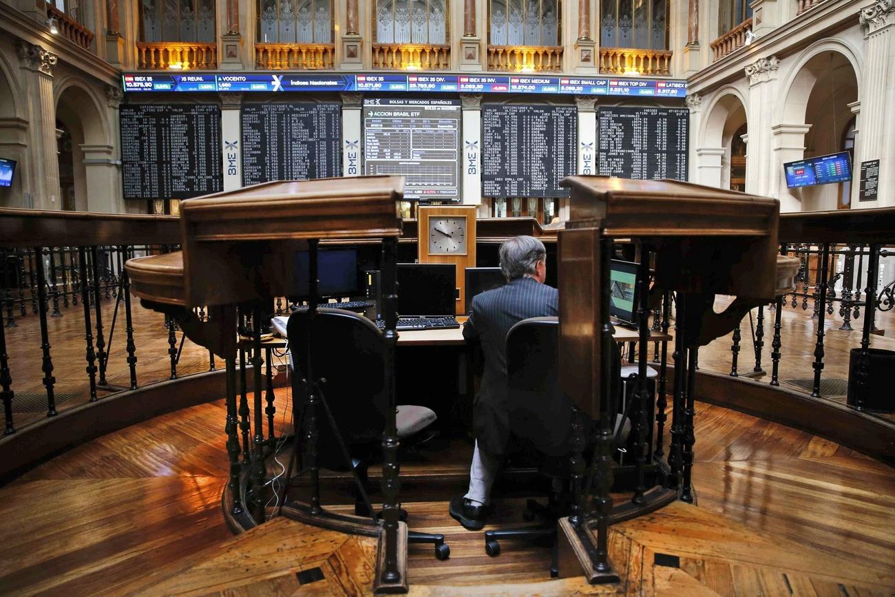 Salone di un palazzo ottocentesco con monitor pieni di nomi e valori numerici; in primo piano uomo seduto a una scrivania