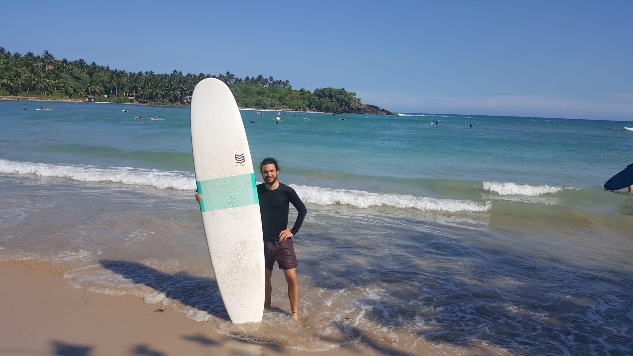 Daniel Gehr mit Surfbrett am Strand.