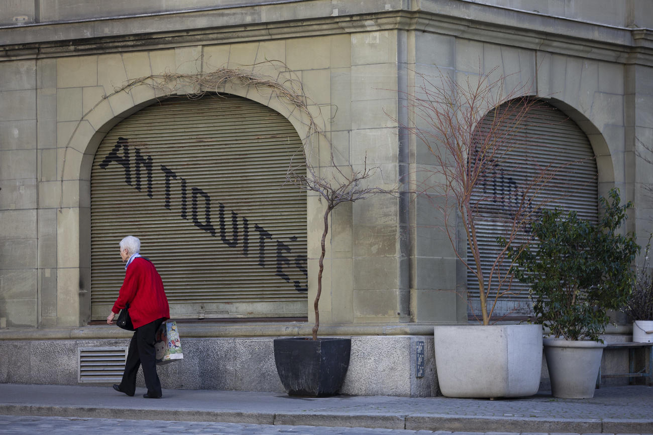 anziana cammina davanti a un negozia con le serrande chiuse