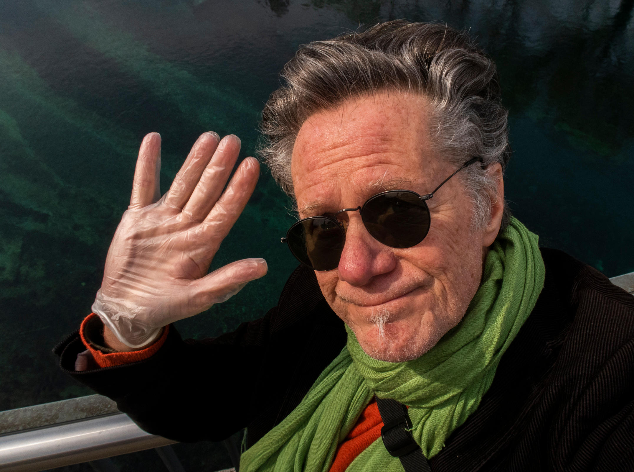 Author in sunglasses, waving to camera with a gloved-hand