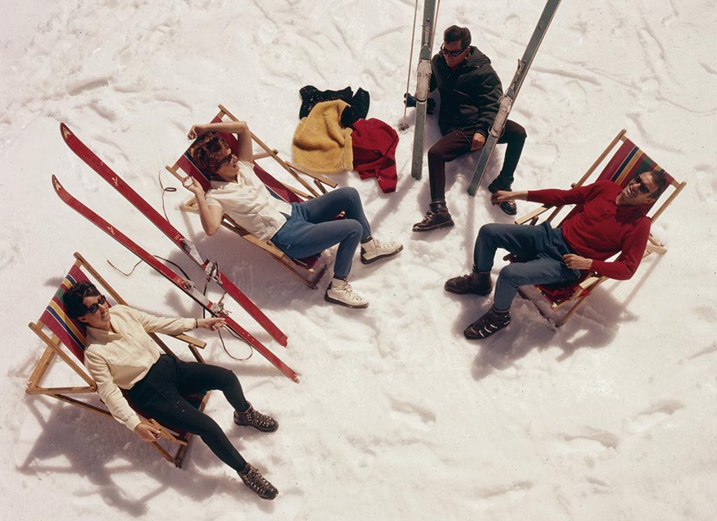 Vier Personen sitzen auf Liegestühlen auf dem Schnee.