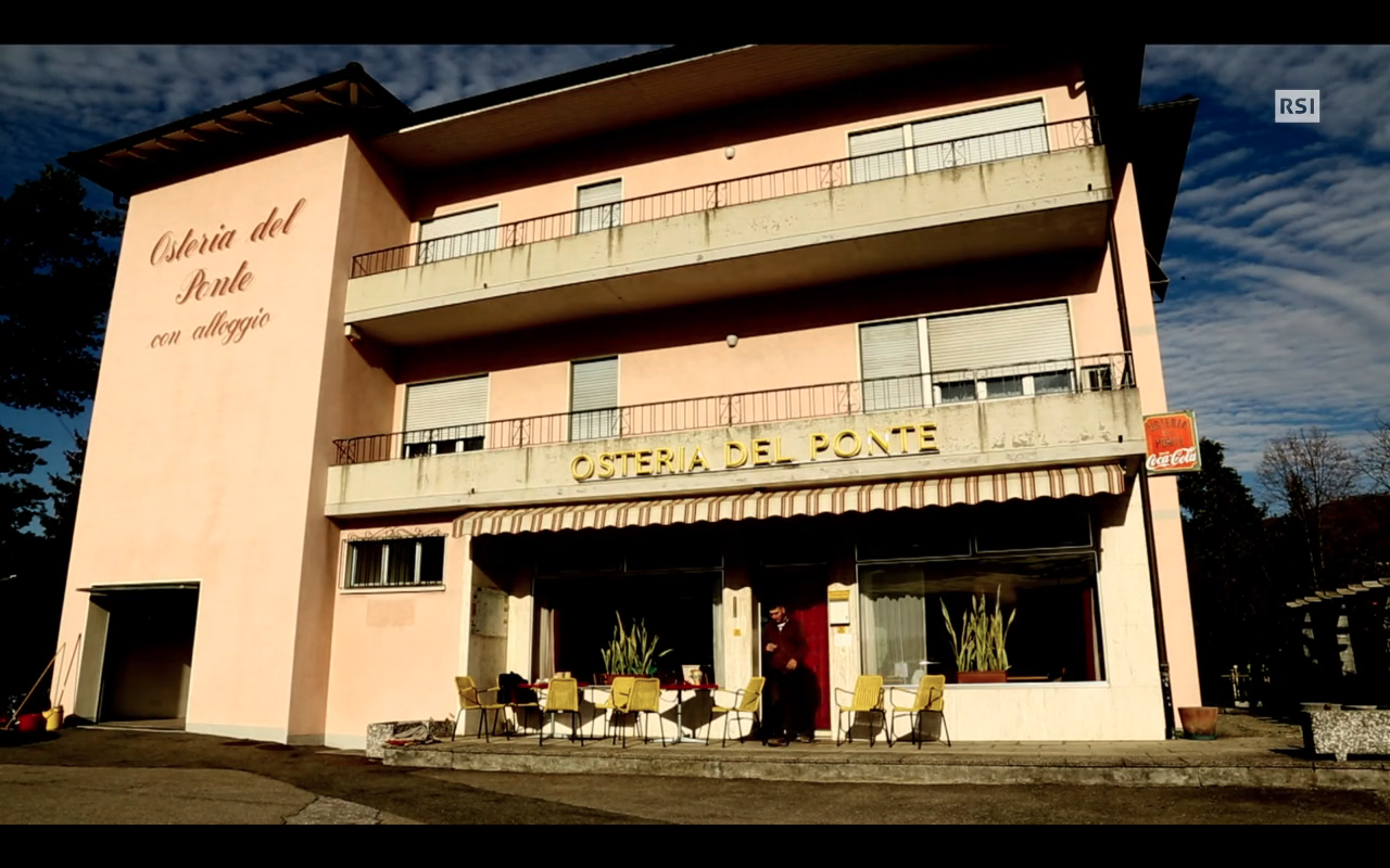 Costruzione a due piani con insegna Osteria del ponte e tavolini e sedie davanti