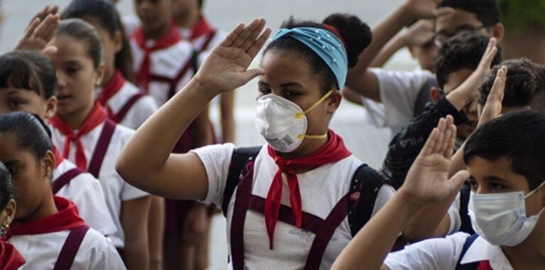 Niños con uniformes escolares alzan la mano, una niña lleva tapabocas