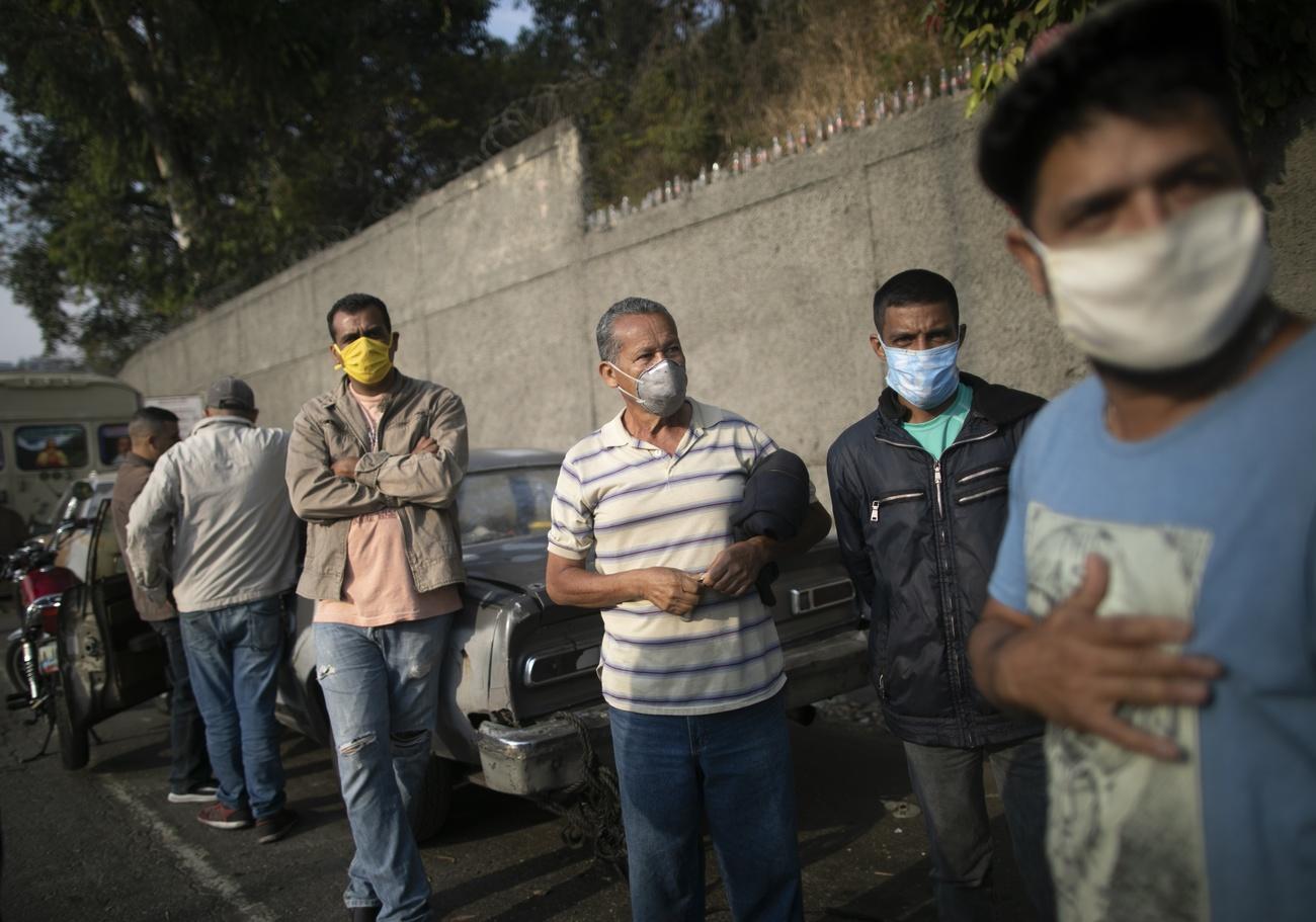 Men queue for gasoline in front of their cars.