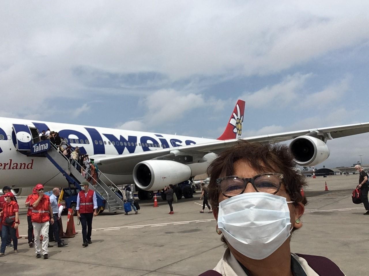 una donna che indossa una mascherina di protezione si fa un selfie davanti a un aereo