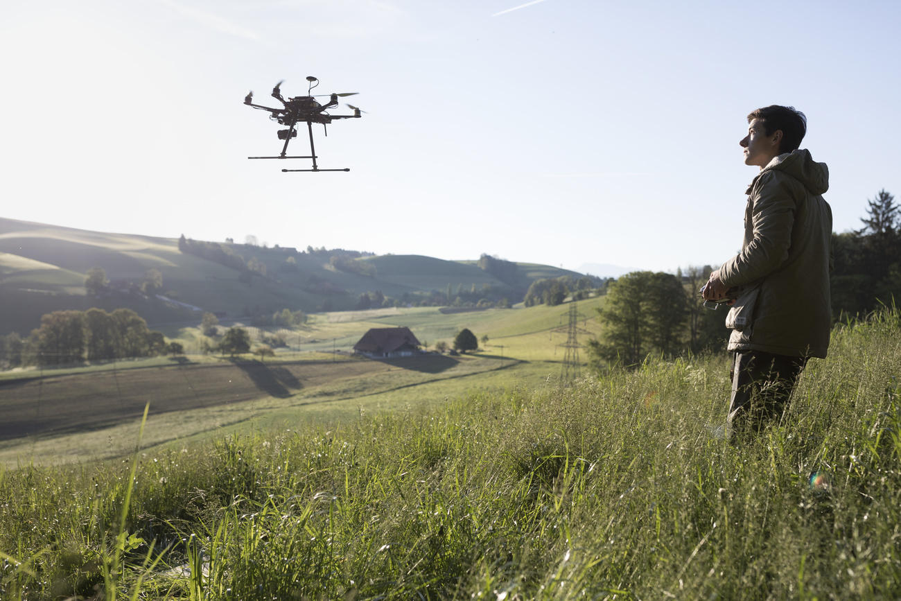 Young man standing in farming field, controls flying drone