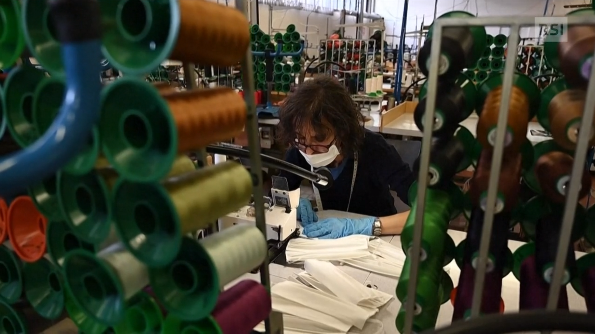 Una donna alla macchina da cucire realizza mascherine chirurgiche in un atelier pieno di rocchetti