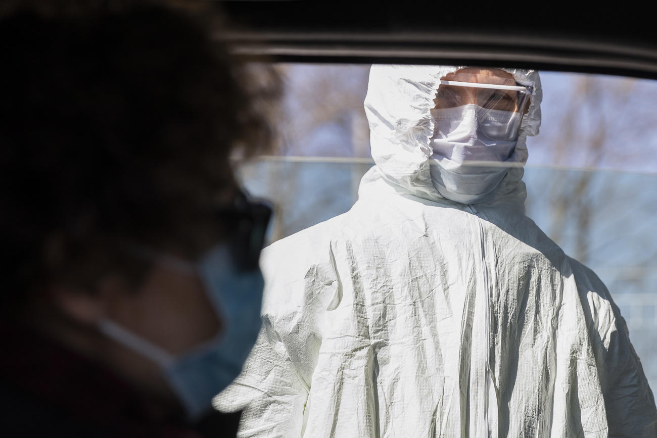 Una donna completamente coperta da protezioni (tuta, mascherina, visiera) vista dall interno di un abitacolo (automobile)