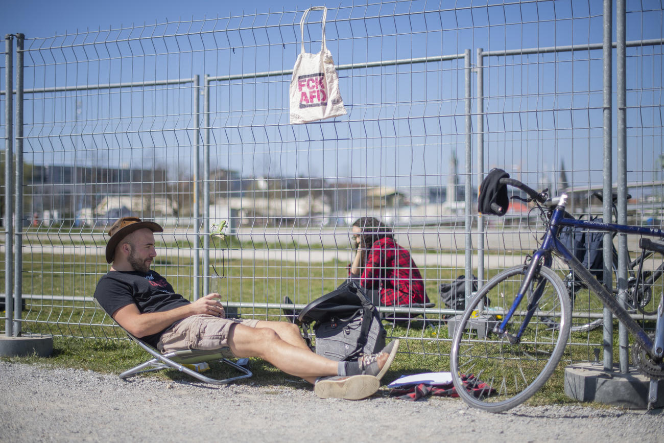 Un giovane con cappello da cowboy e una giovane oltre una doppia barriera metallica si parlano in un parco soleggiato