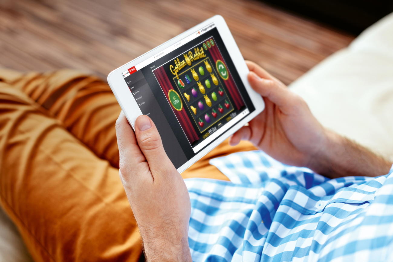Ein Mann hält ein Tablette in beiden Händen, auf dem eine Slotmaschine abgebildet ist.