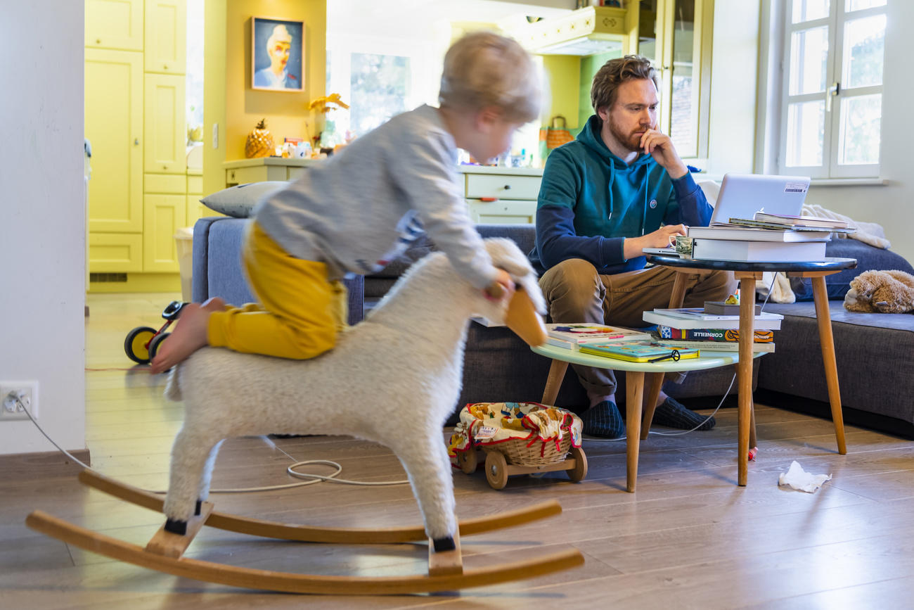 un bambino su un cavallo a dondolo e un uomo seduto a un tavolino che lavora al computer