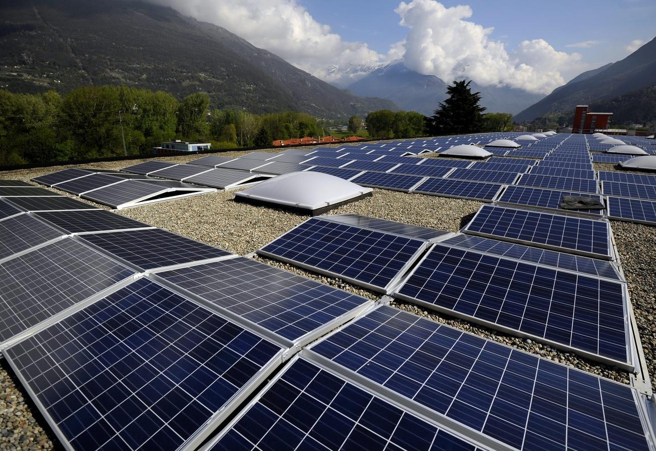 Tetto di edificio industriale quasi interamente coperto da pannelli in contesto prealpino con cielo parz. nuvoloso