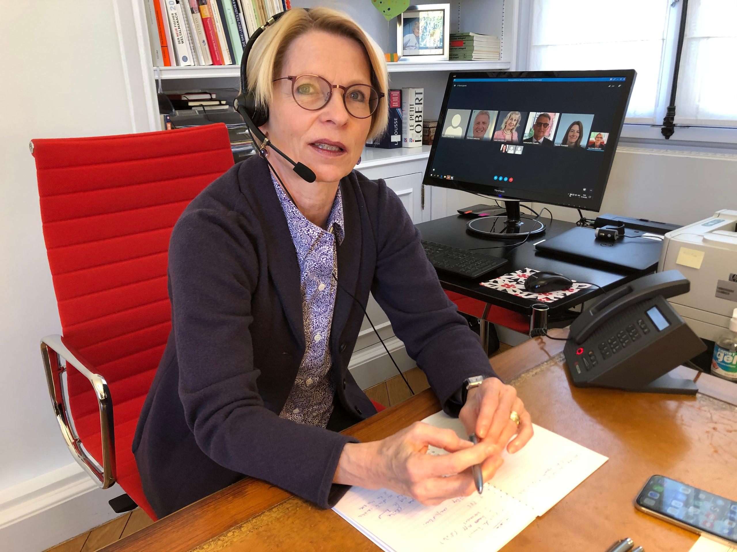 Frau mit Kopfhörern an einem Schreibtisch, im Hintergrund ein Bildschirm.