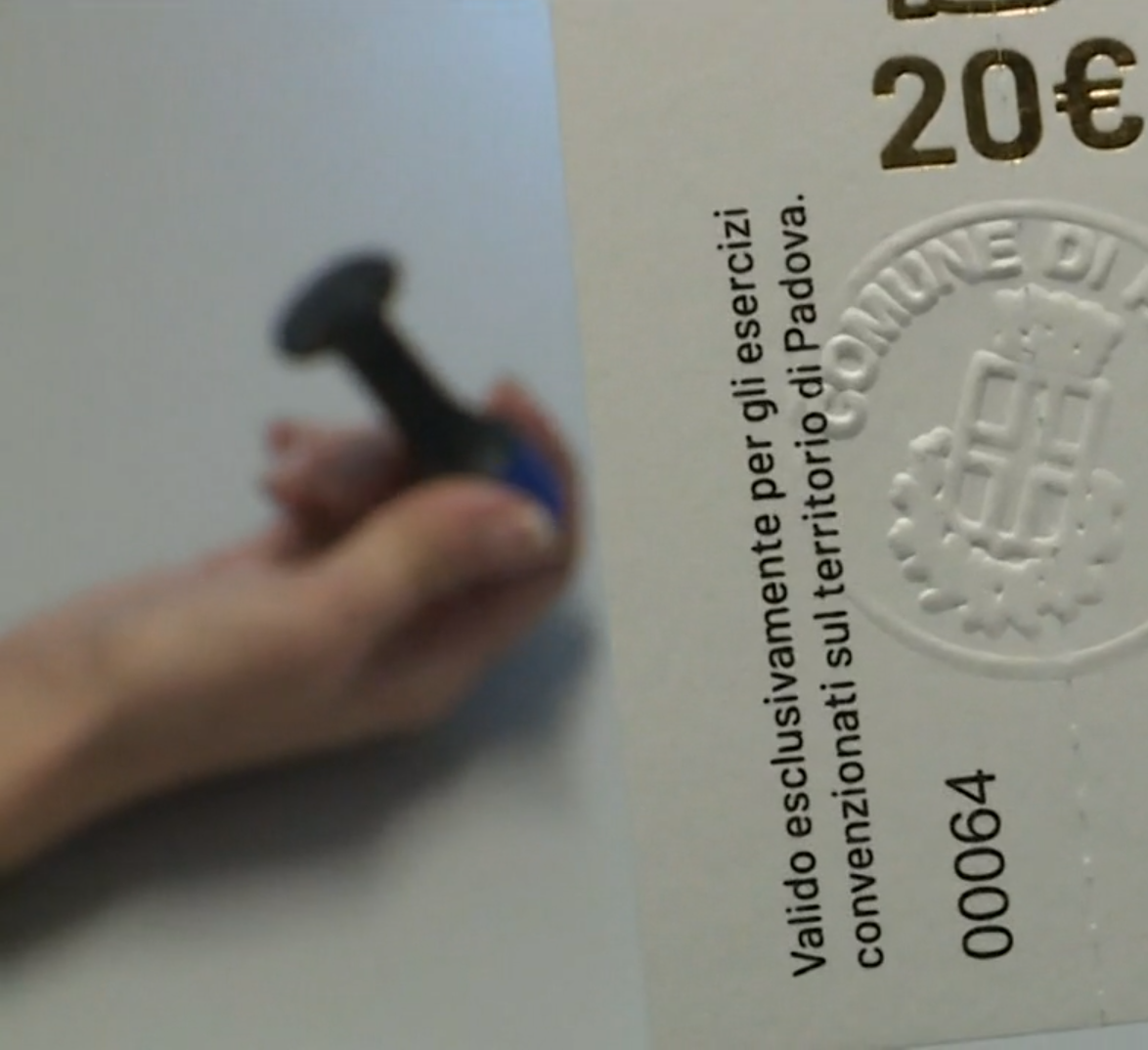 Primo piano di un buono alimentare da 20 euro del Comune di Padova, si intravvede mano che tiene un timbro o sigillo