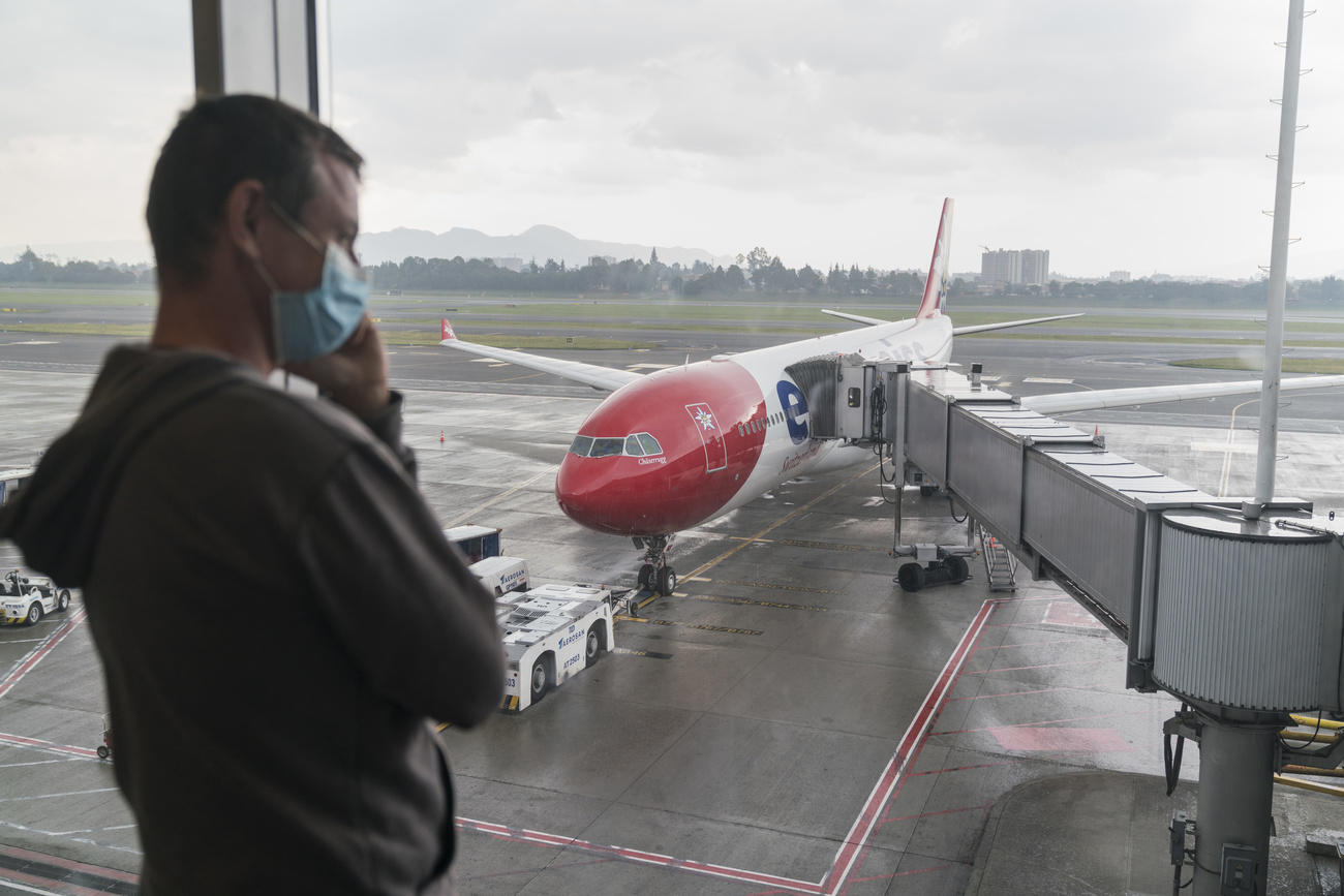 Ein Mann mit Gesichtsmaske vor einem Fenster, draussen steht ein Flugzeug.