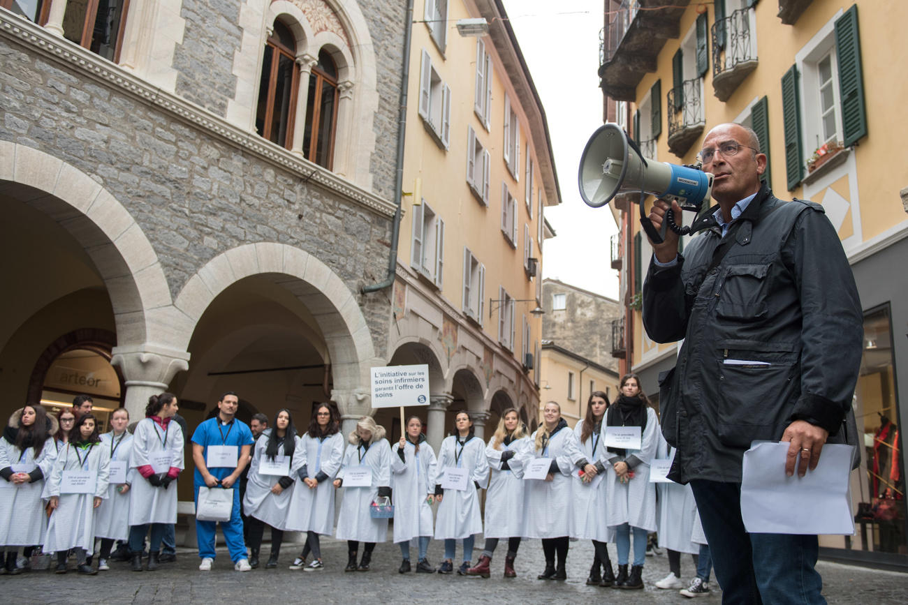 homme avec un mégaphone devant des femmes en blouse blanche