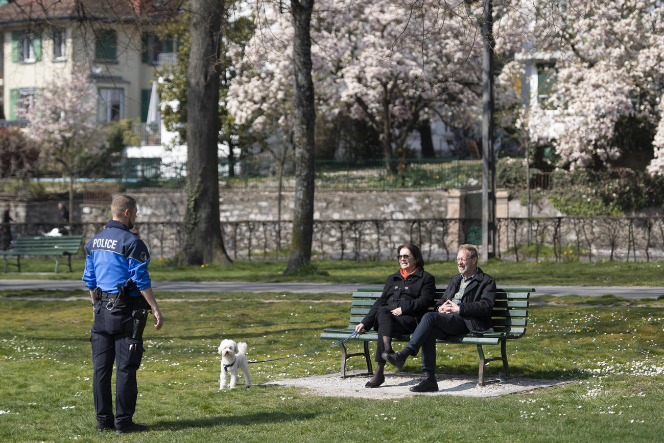 Ein Polizist spricht mit zwei Menschen, die auf einer Bank sitzen.