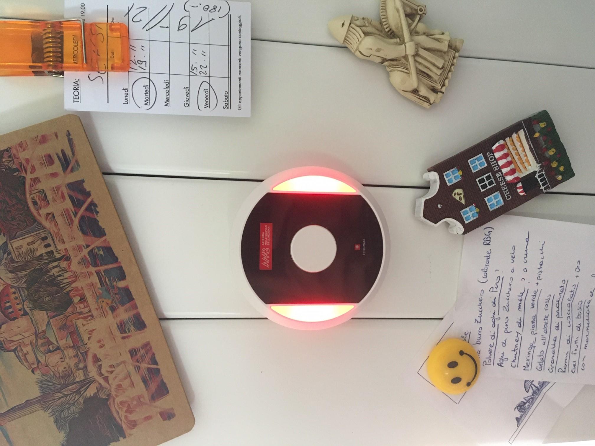 Alcuni oggetti magnetici attaccati a un calorifero piatto; tra questi, un disco con scritta AMB e fasce luminose rosse.