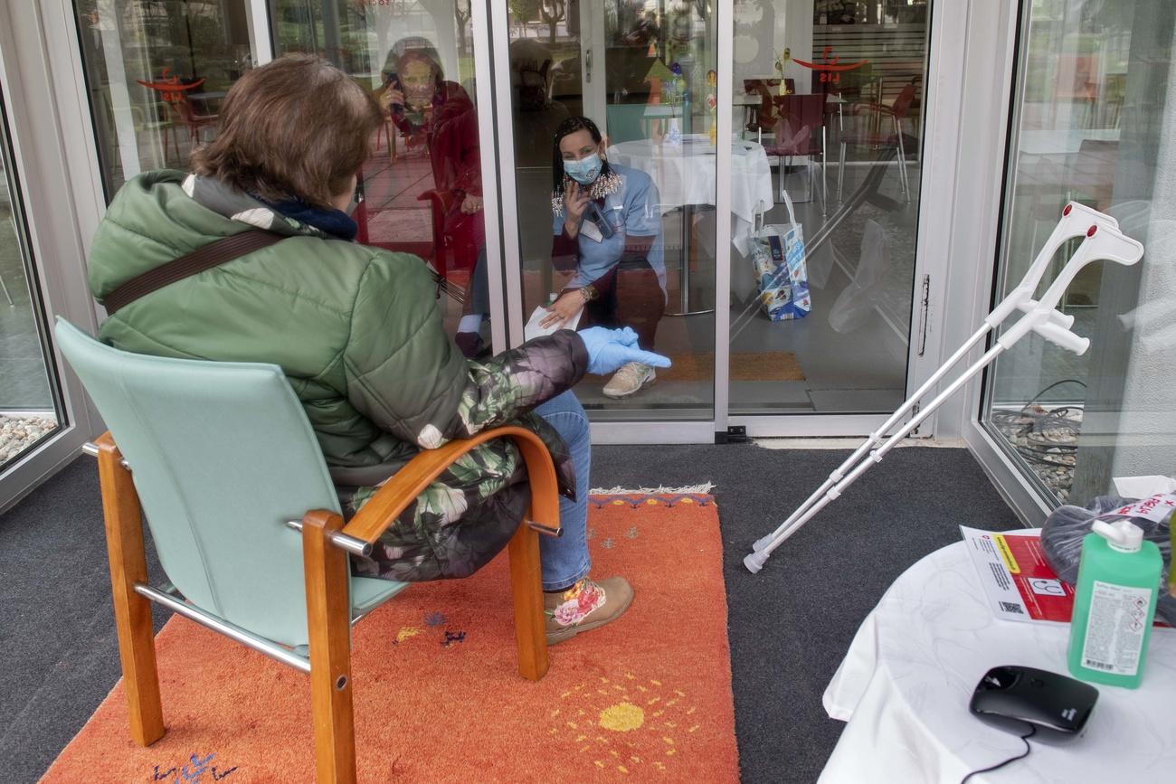 residencia para mayores: Una señora habla por teléfono y con un vidrio de por medio, con una joven