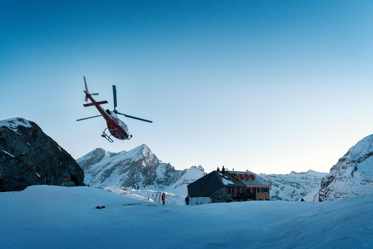 Ein Helikopter fliegt zu einer Hütte im Schnee.