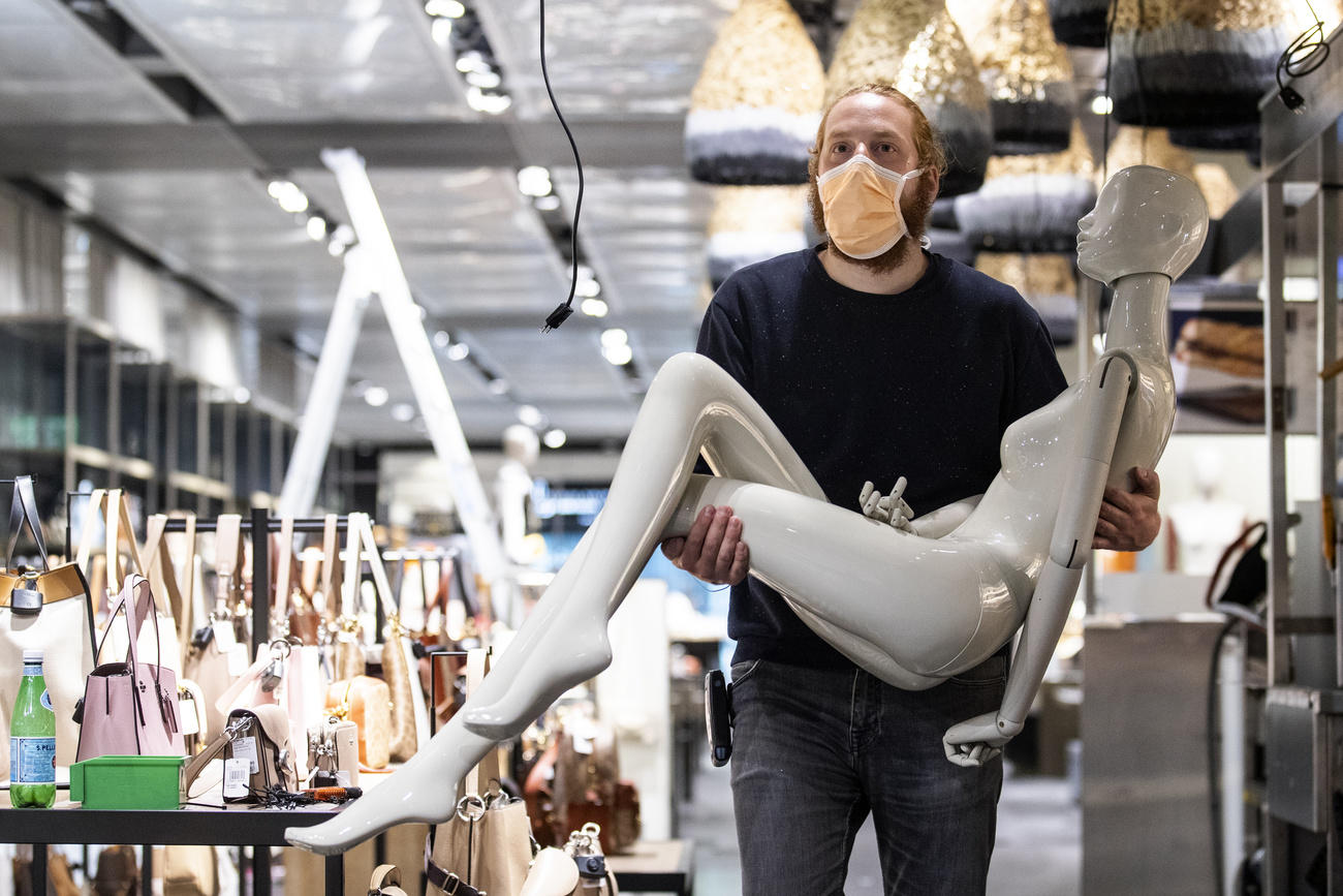 Un hombre con mascarilla protectora lleva entre los brazos un maniquí.