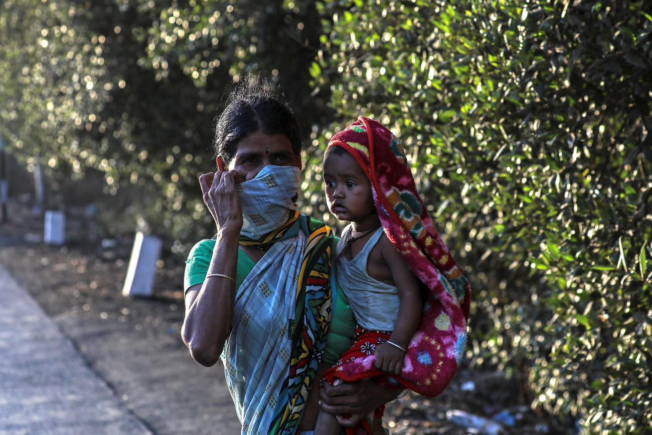 Trabajadora migrante de la India con su bebé en brazos y una mascarilla facial