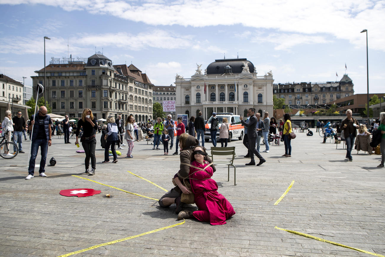 Due persone con abiti di scena sedute e legate l una a all altra in mezzo a un ampia piazza.