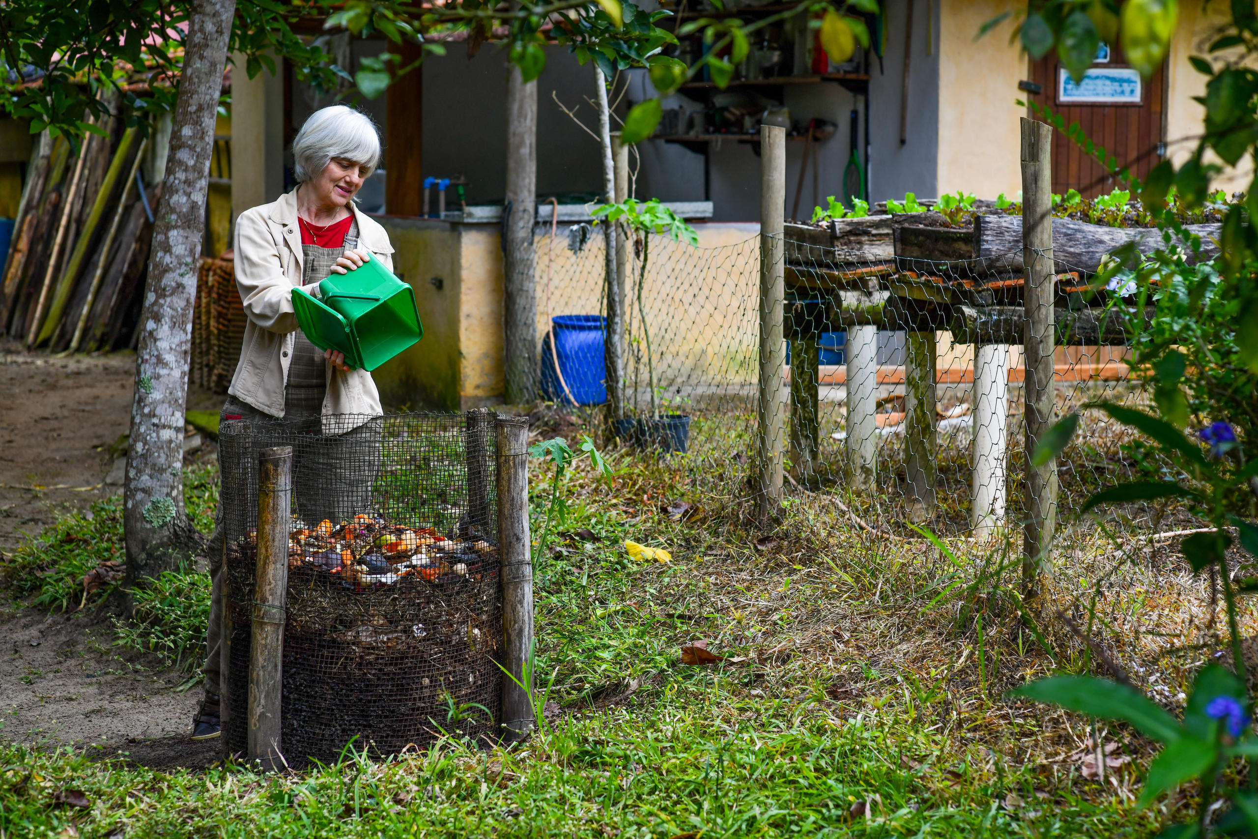 una donna svuota un contenitore nella compostiera da giardino.