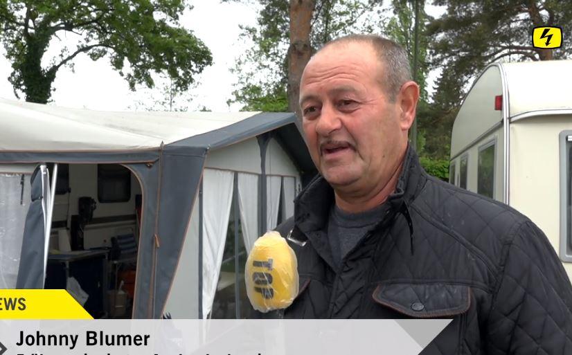 Ein Mann spricht vor einem Wohnwagen in ein Mikrofon.