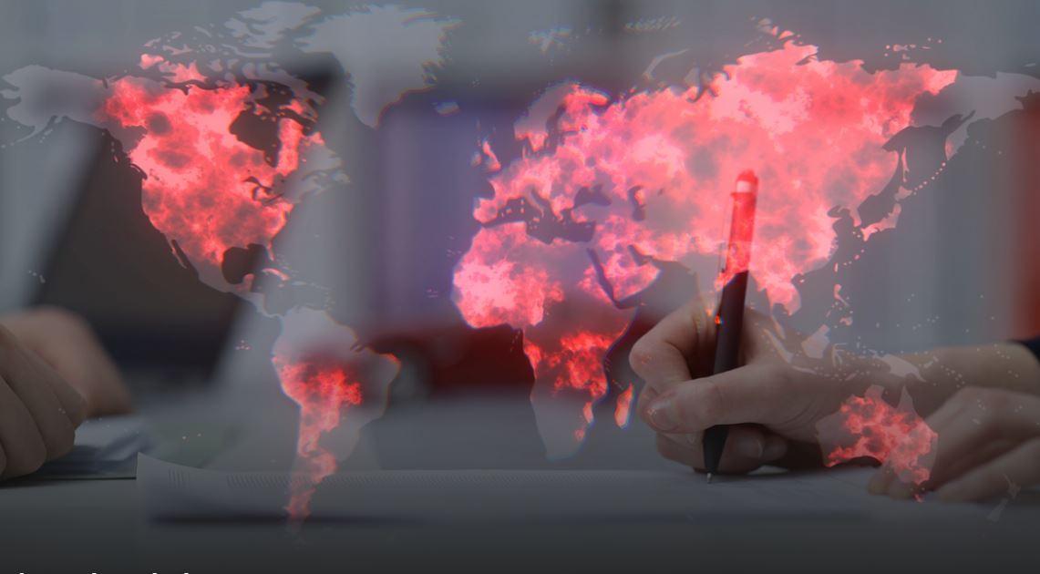Un fotomontaggio con dietro la mappa del mondo e in primo piano una mano con una penna che sta scrivendo