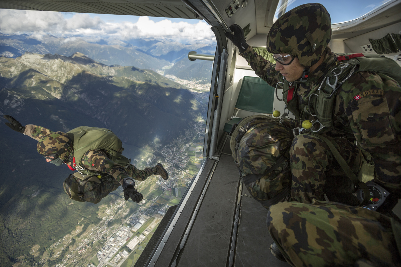 Interno di un piccolo aereo con portellone aperto; un militare si è appena lanciato in paracadute, un altro guarda