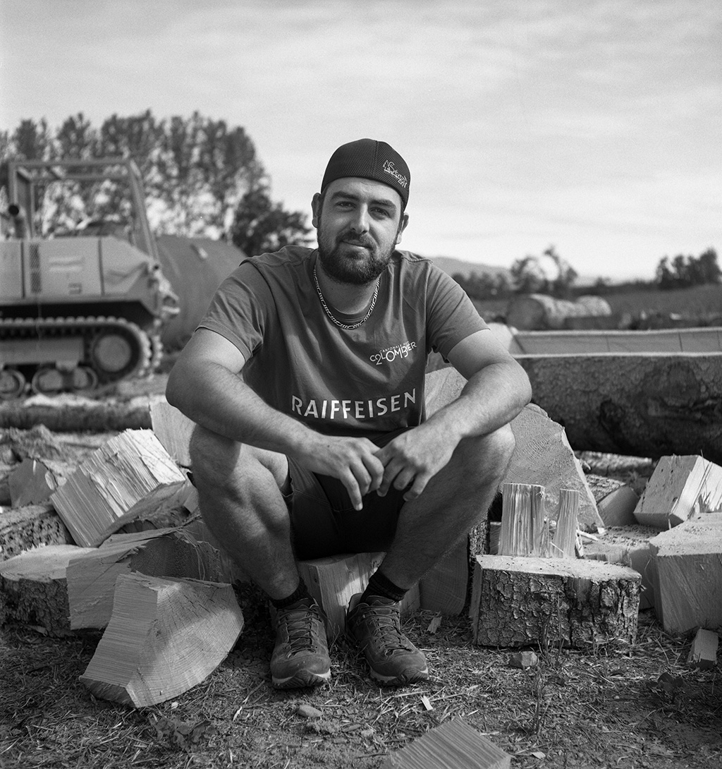 Young man wearing a reversed baseball cap, crouches on the ground, looking directly to the camera.