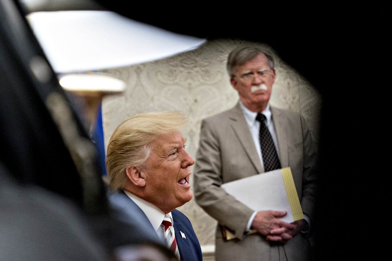 Donald Trump che parla e John Bolton che ascolta con alcuni fogli in mano intravisti attraverso un varco