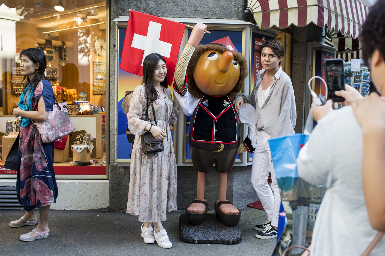 Turistas se toman una foto junto a un muñeco de madera, a la entrada de una tienda