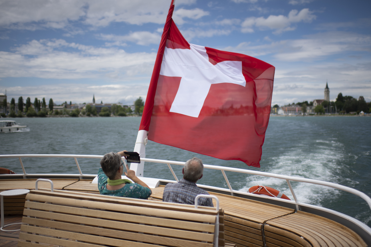 Blick von einem Schiff mit Schweizer Fahne auf einen See und eine Stadt im Hintergrund.