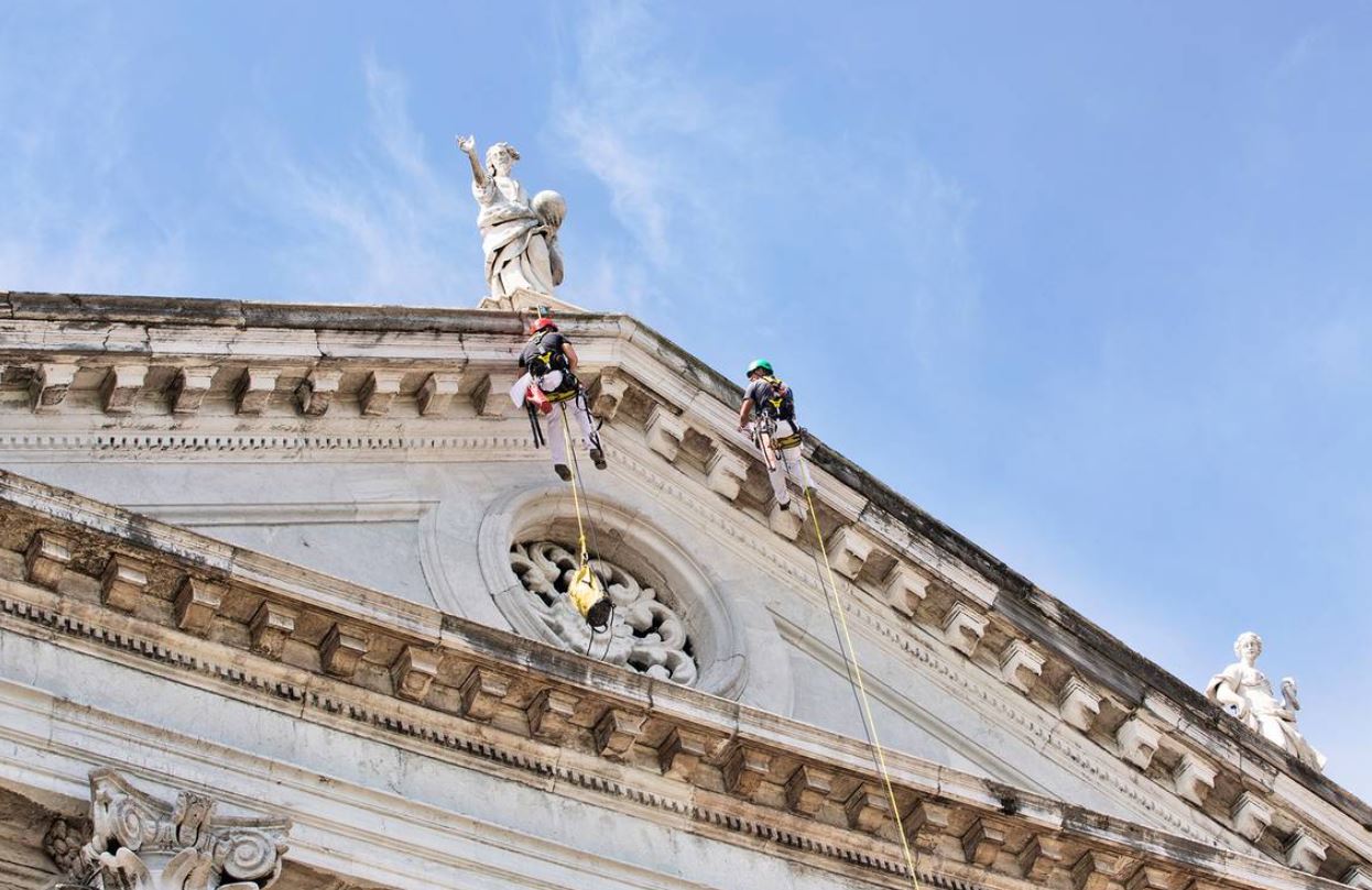 La facciata della chiesa con due restauratori appesi nel vuoto