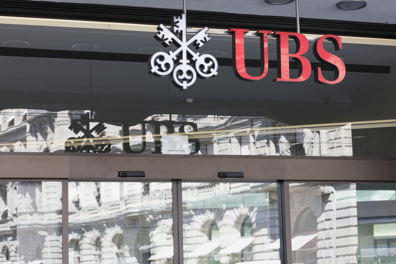 Dettaglio di porte scorrevoli sovrastate da insegna UBS, specchiano palazzo di fronte