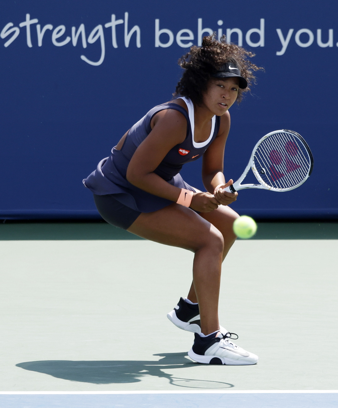 Tennista donna immortalata un istante prima di colpire la pallina; vestita di blu, sfondo blu