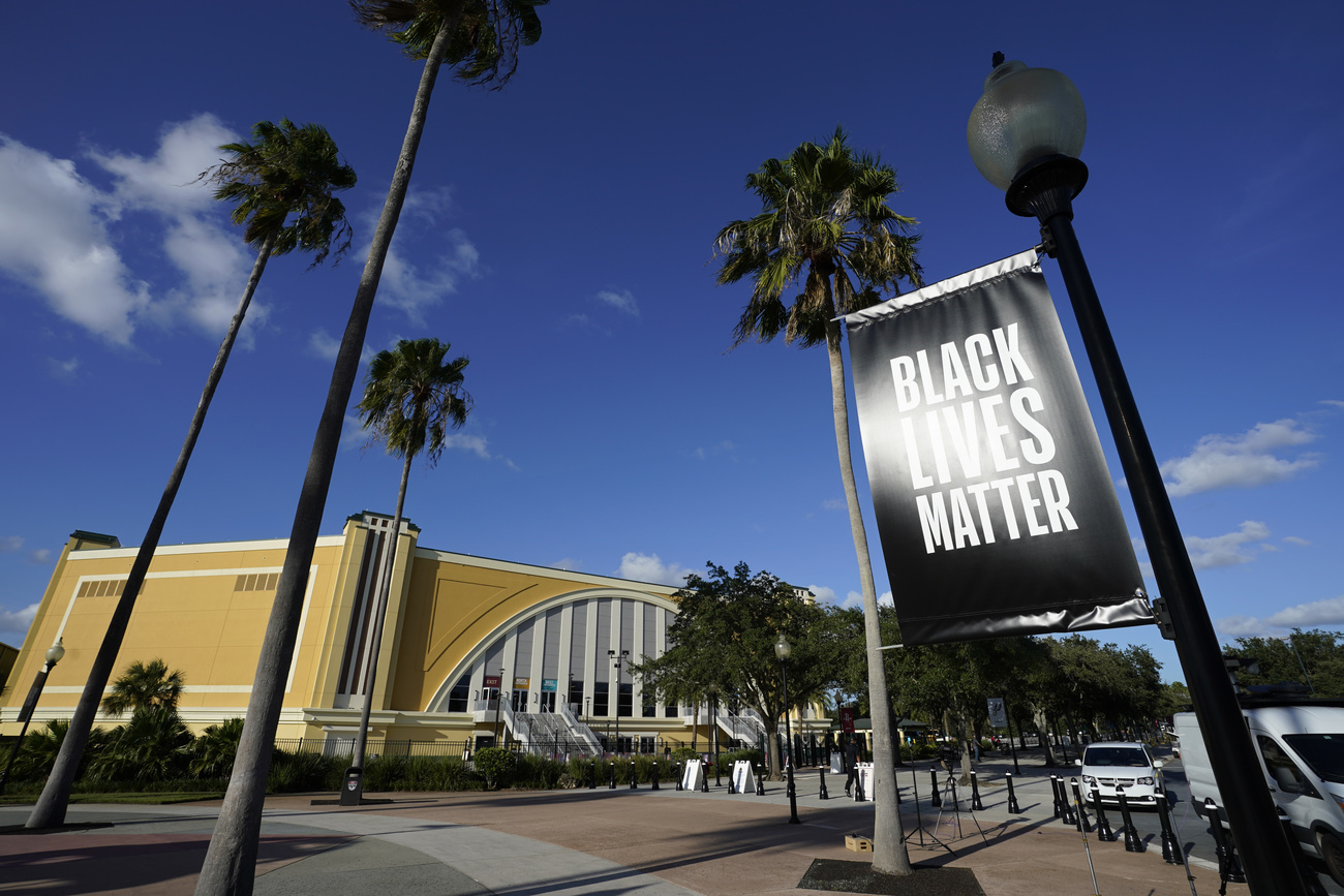 Esterno di un palazzetto dello sport con palme, parcheggi e un cartelli Black Lives Matter