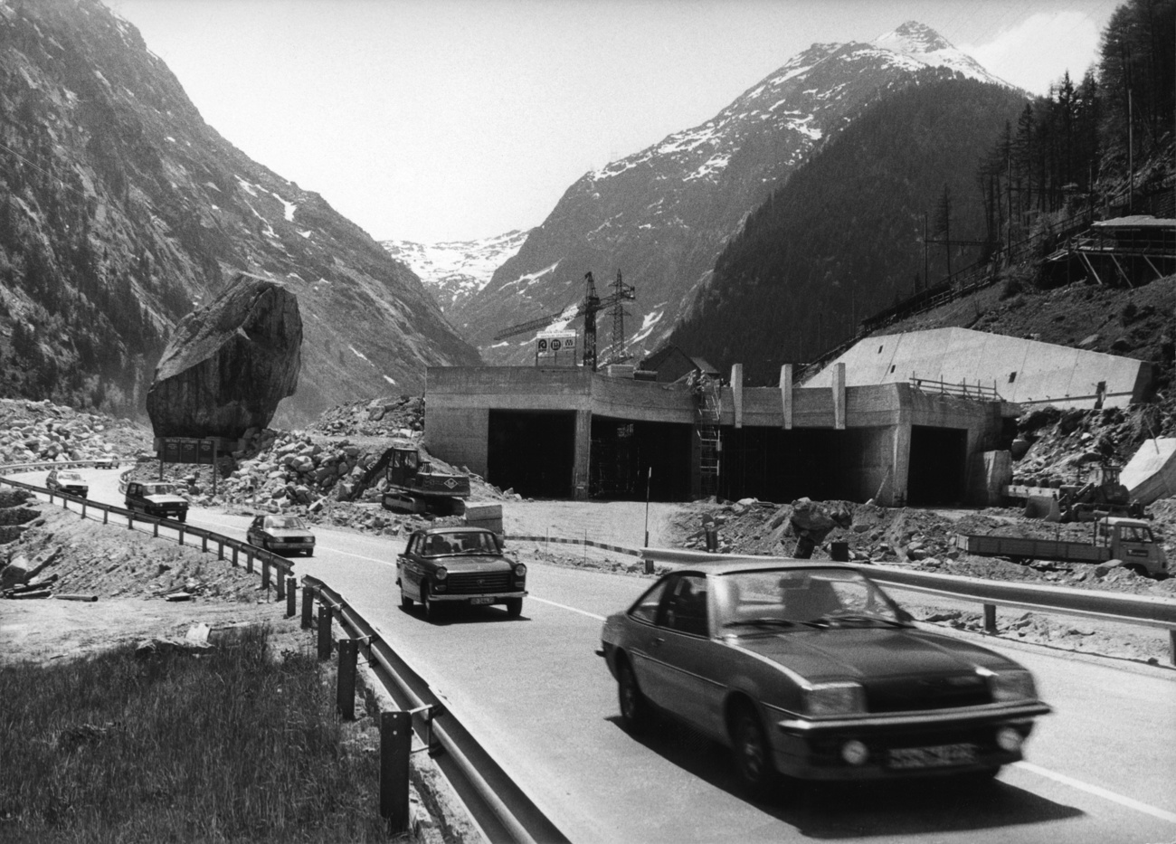 Noch im Bau befindliches Tunnelportal in alpiner Umgebung, links ein grosser Felsbrocken