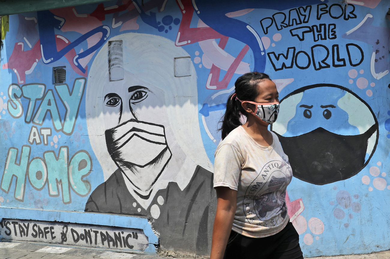 Una ragazza con mascherina passa davanti a un murale che raffigura donna con mascherina e messaggi di prevenzione