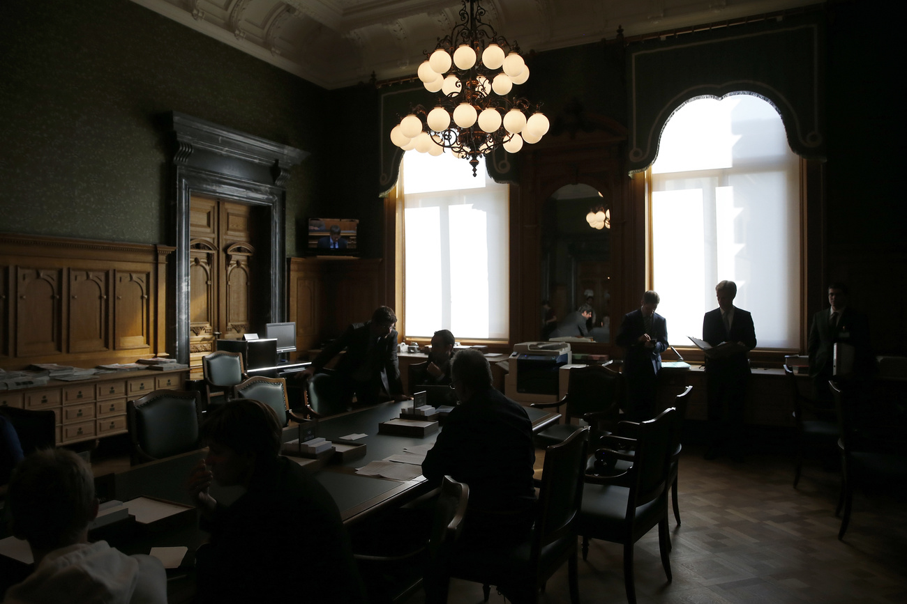 Politicians and lobbyists sit in a dark room with chandelier