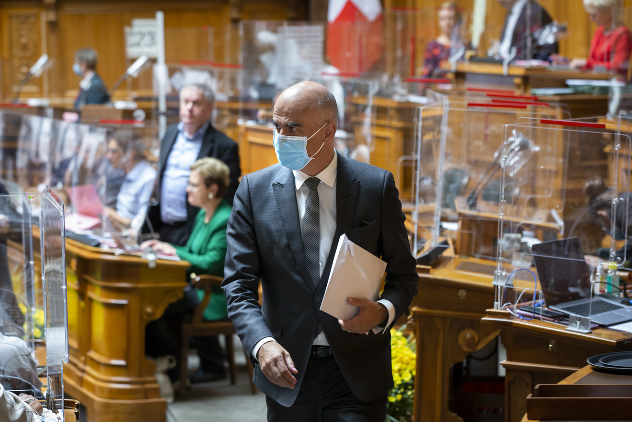 رجل يرتدي كمامة ويحمل وثائق داخل قاعة الجلسات بالبرلمان