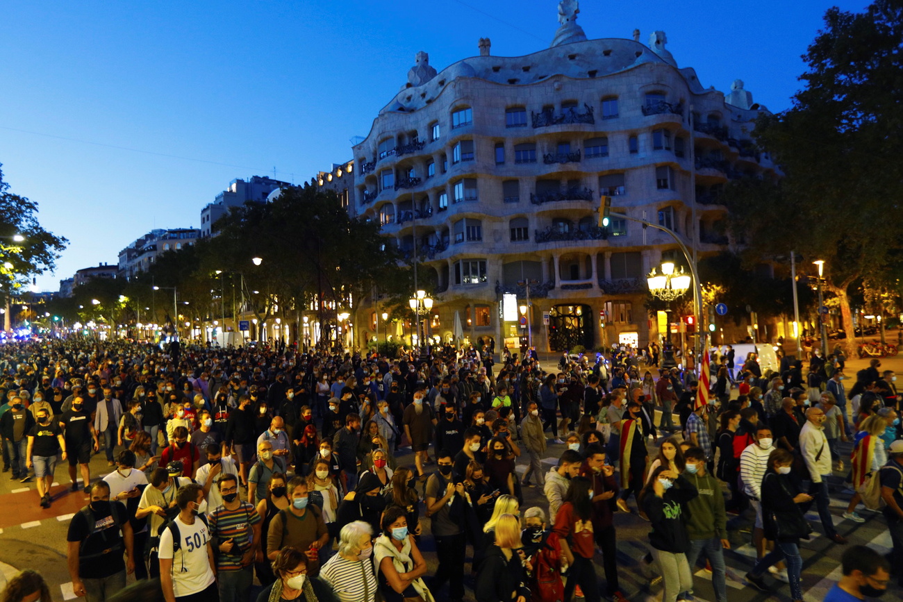 Folla di manifestanti al crepuscolo davanti a quella che si riconosce essere una famosa costruzione di Gaudì a Barcellona