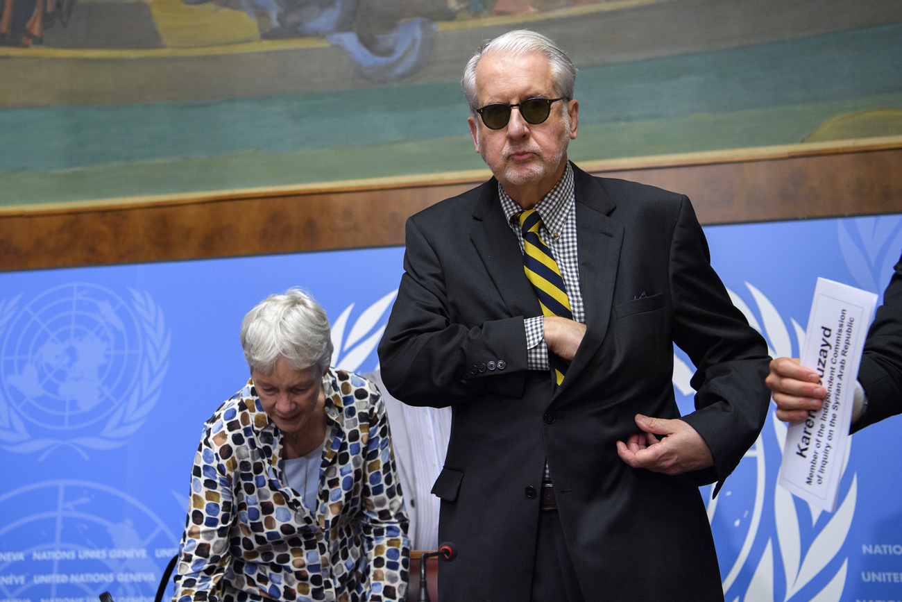 رجل طويل القامة يرتدي نظارات سوداء وبجانبه امرأة وفي الخلفية علم الأمم المتحدة