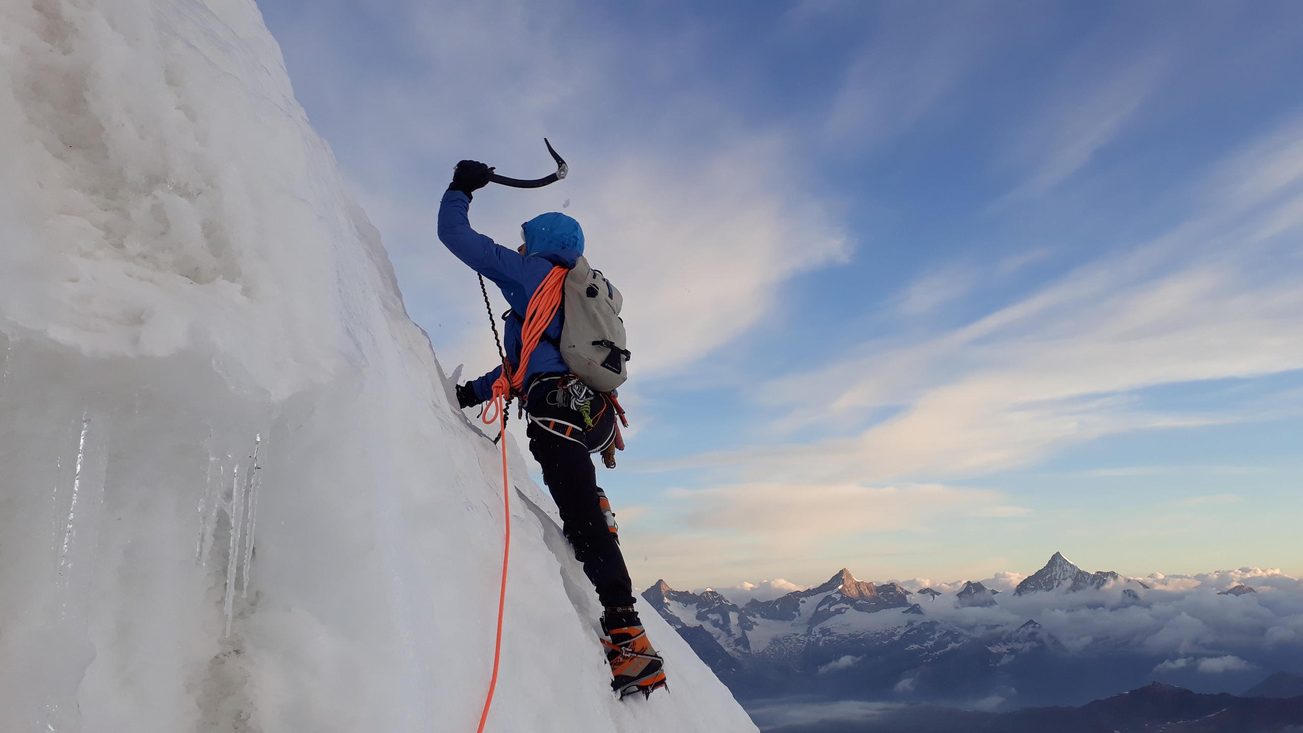 Climber on a mountain wall, attached to rope, about to strike with an ice axe